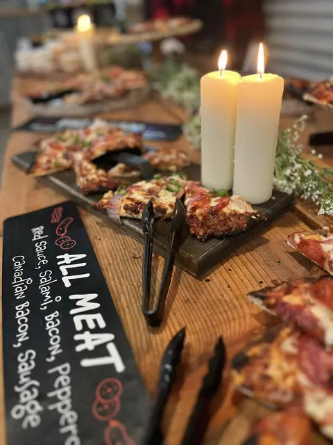 Pizza slices on serving boards beside candles and an All Meat sign