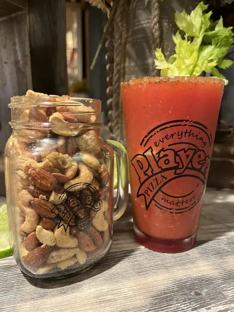 Players Pizza mug of Bloody Mary beside a jar of mixed nuts